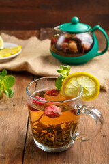 green tea in a glass cup with strawberries mint and lemon on a wooden table and a teapot and lemon in a plate and mint leaves.
