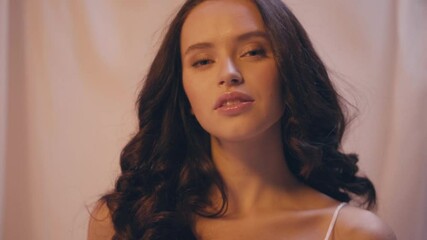 slow motion of sensual woman adjusting wavy hair and looking at camera on white - Powered by Adobe