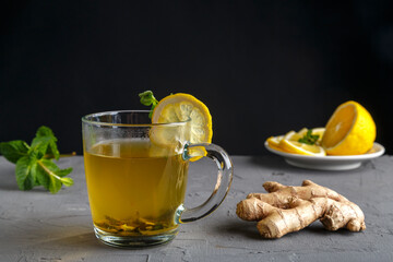 vitamin ginger drink with honey mint and lemon in a glass cup near ginger root and lemon on a concrete background.