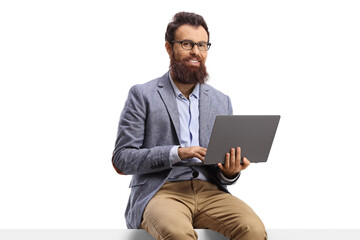 Bearded man seated on a blank panel with a laptop