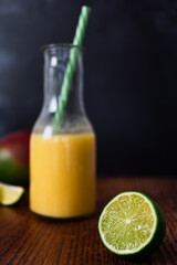 Drinks photography shot of fresh fruit smoothie seen out of focus in background with fresh and jiucy lime segment in crisp focus in foreground. Dark background with copy text space available