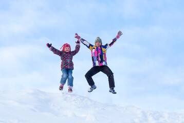 Winter activities outdoors. Happy expressive little girls wearing a warm clothes jumping and enjoying life against the blue sky on a snow in winter
