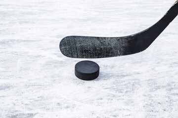 Black hockey stick and rubber puck on ice background. Closeup. Front view.