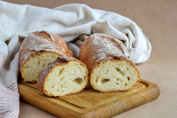 Bread loaf, cut into pieces, on wooden cutting board. Baked bread and dish towel on craft paper, home baked loaf. Organic healthy eating. Close-up. Selective focus.