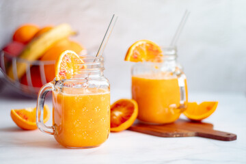 Homemade spring detox smoothie from oranges, carrots and banana in mason jar and glass straw