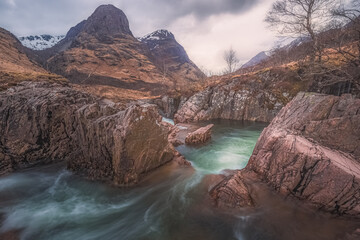 Hidden waterfall landscape along the River Coe flowing towards mountain peaks of Beinn Fhada, Gearr Aonach, Aonach Dubh (the Three Sisters of Glencoe), in the Scottish Highlands.