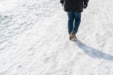 Man walking on compacted snow wearing anti slip rubber boot covers, with stud spikes for grip