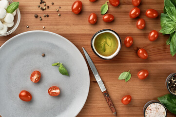 Mozzarella and cherry tomatoes with basil leaves, salt and pepper, layout on a wooden board. The process of preparing Italian Caprese salad. Top view