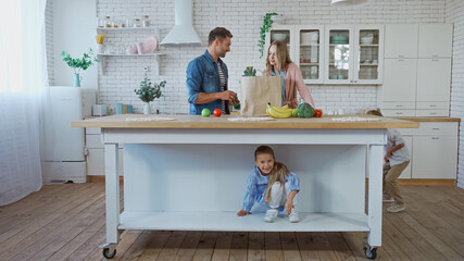 Children playing in kitchen near parents with food and paper bag