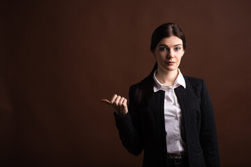 Portrait of serious brunette business woman pointing her thumb to the side in studio on brown background with copyspace