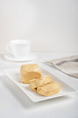 Halva, also halvah or halwa is Turkish homemade dessert made of sesame oily seeds grinded to a paste and mixed with sugar syrup served on white plate on wooden table with towel and cup. Vertical