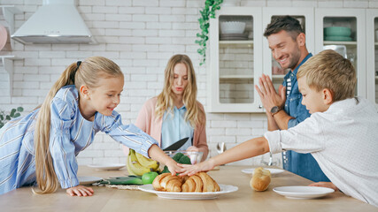 Children taking croissants near parents on blurred foreground in kitchen