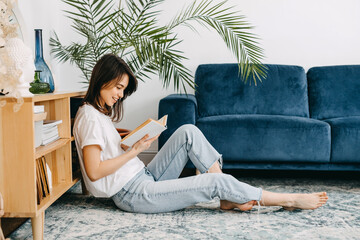 Young woman reading a book at home, sitting on the floor.