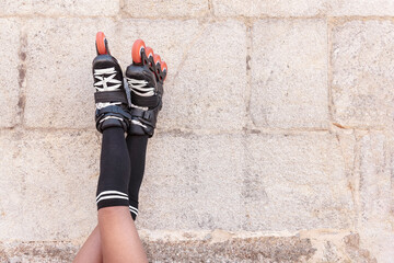 Close-up of legs up high with inline skates leaning against a stone wall resting for later...