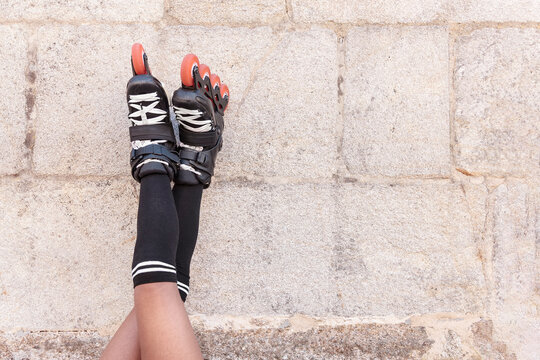 Close-up of legs up high with inline skates leaning against a stone wall resting for later training, skating outdoors and playing sports on a hot summer day