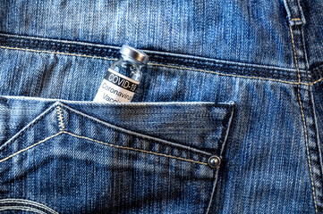 Medical vial for injection in blue jeans pocket. Glass ampoule with the inscription COVID-19 VACCINE