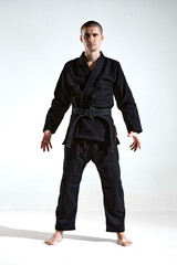 Confident frowning male in black kimono for karate or kudo on white studio background with copy...
