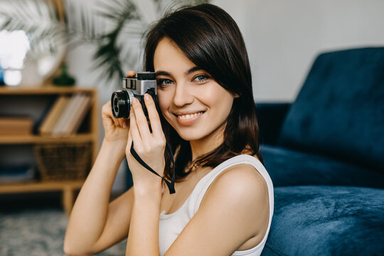 Young brunette woman, smiling, taking pictures with a vintage film camera at home.