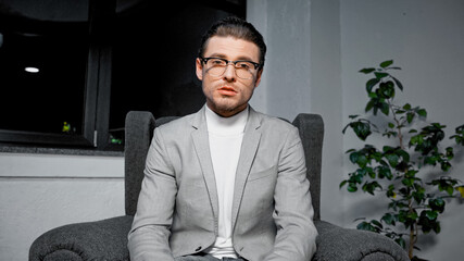 Manager in eyeglasses looking at camera while sitting in armchair in office