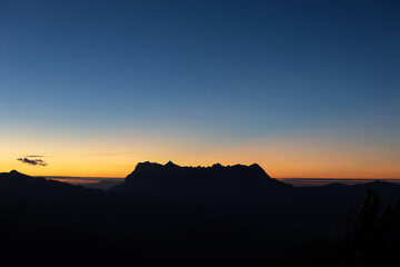 Heaven at early morning with copy space and silhouette mountains.Predawn clear sky with orange horizon and blue atmosphere. Smooth orange blue gradient of dawn sky.