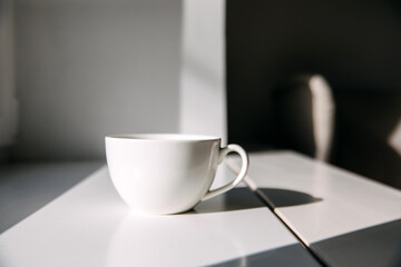 Blank white mug of coffee or tea on windowsill in sunlight.