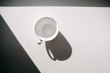 Empty white cup on windowsill in sunlight, top view.