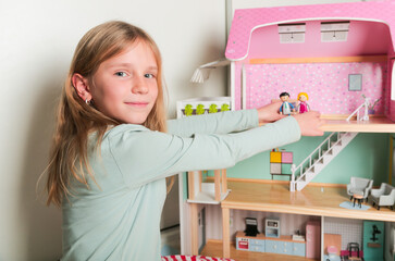 Fototapeta na wymiar Happy girl plays with doll house and dolls. Happy child.