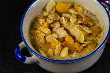 Overnight oats bircher topped with toasted almond flakes, peach and honey, closeup.