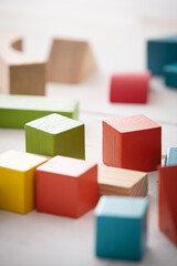 Games with colorful wooden bricks on a white wooden table. The child plays with geometric shapes made of natural wood. Learning and education concept.