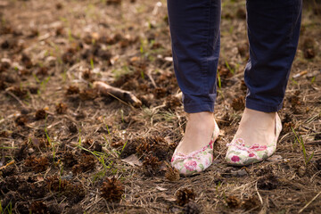 Closeup of legs of a young woman in jeans and pumps. Dry spruce needles and cones lie on the ground. Spring in the park. in the fresh air.