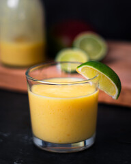 A close straight on shot looking of a glass of fruit juice or smoothiewith lime segment on side. Jar or bottle of juice and fresh fruit in background. Copy space available