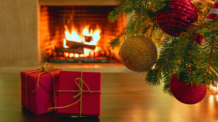 Xmas tree branch with balls, red gift boxes, blur burning fireplace background.