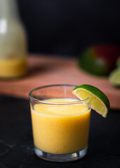 A close straight on shot looking of a glass of fruit juice or smoothiewith lime segment on side. Jar or bottle of juice and fresh fruit in background. Copy space available