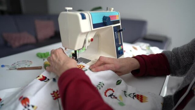 Process of tailoring working , hands of elderly seamstress sews clothes with needle, looper and presser on a sewing machine. Small home business concept