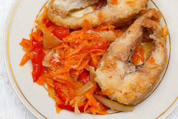 Pieces of fried pike with a vegetable garnish of bell peppers, onions and carrots on a round white plate.