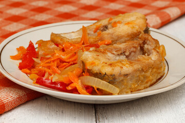 Pieces of fried pike with a vegetable garnish of bell peppers, onions and carrots on a round white plate.