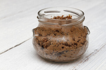Chicken liver pate with prunes and apple in a glass jar on a white wooden background.