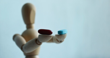 Wooden figurine of a man, holding two pills, on a light background with free space for your text. Medicine and healthcare concept.