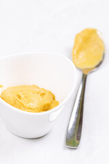 Mustard on the metal spoon above white background