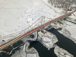 Aerial drone view. Pedestrian bridge over the frozen Dnieper River in Kiev. Cloudy frosty winter morning, frosty pattern on ice.