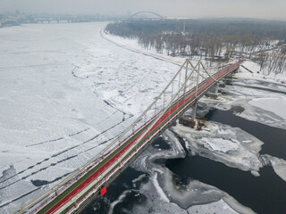Aerial drone view. Pedestrian bridge over the frozen Dnieper River in Kiev. Cloudy frosty winter morning, frosty pattern on ice.