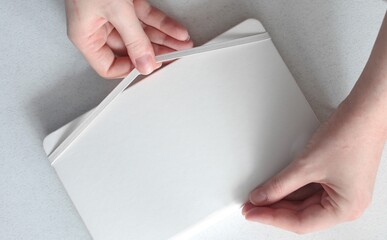 Woman opens a white leather notebook fixed with an elastic on a light gray backpround. Flat lay....