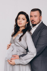 Pregnancy photoshoot of a beautiful couple, future parents in a gray dress and suit