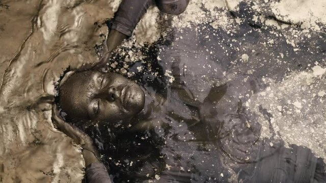 A woman dives into the water lying on her back, covered all over with gold paint. He lies with his eyes closed.