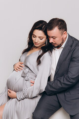 Pregnancy photoshoot of a beautiful couple, future parents in a gray dress and suit