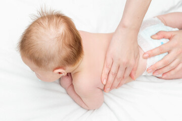 Three month baby boy receiving back massage from a female massage therapist. Relaxing newborn kid. Close up. The masseur gives the child a back massage