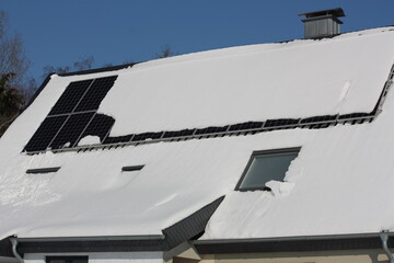 Fototapeta na wymiar Photovoltaikanlage auf völlig verschneitem Dach bei blauem Himmel