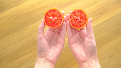 Slice of red blood orange in hands on a wooden table background