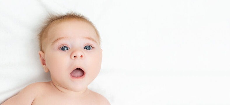 Portrait of an astonished cute newborn baby. The boy a surprised expression. Newborn lying on a white background. Kid with open mouth. Top view. Banner. Copy space.