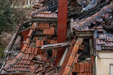 House Rooftop Fire Damage. Charred roof trusses and burnt furniture. A blazing fire burns through the roof rafters.
